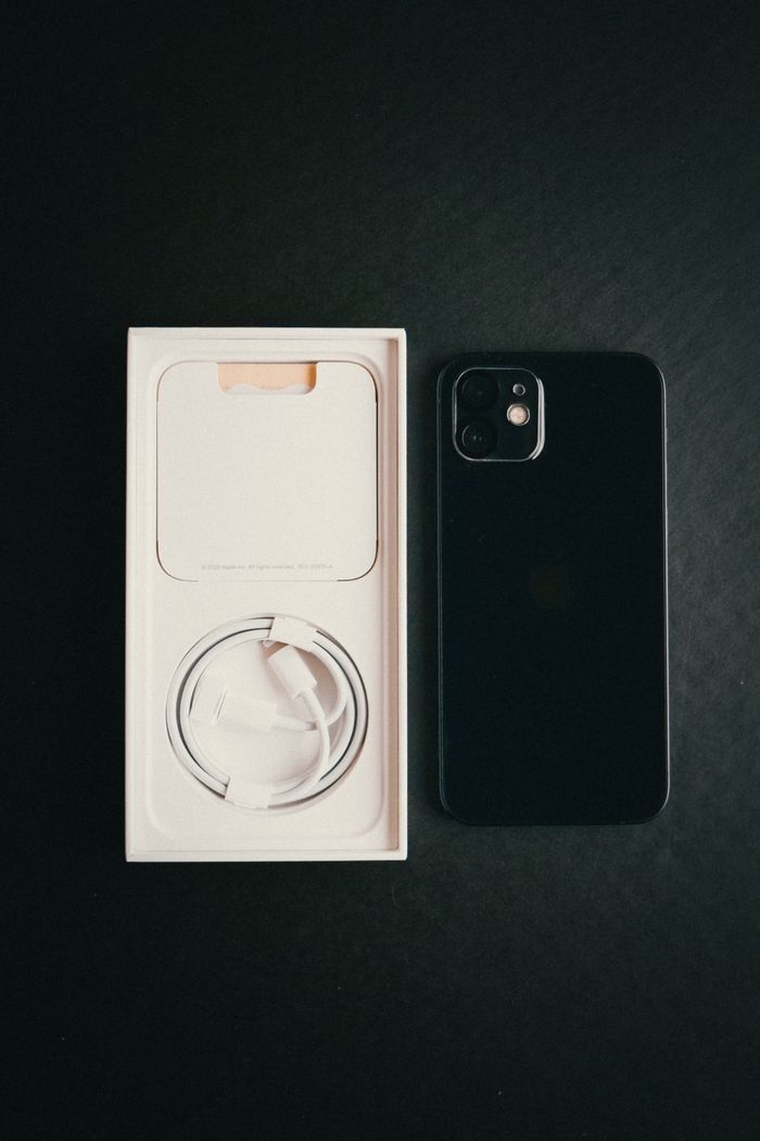 Services High-angle shot of a smartphone, charger cable, and box on a dark surface.