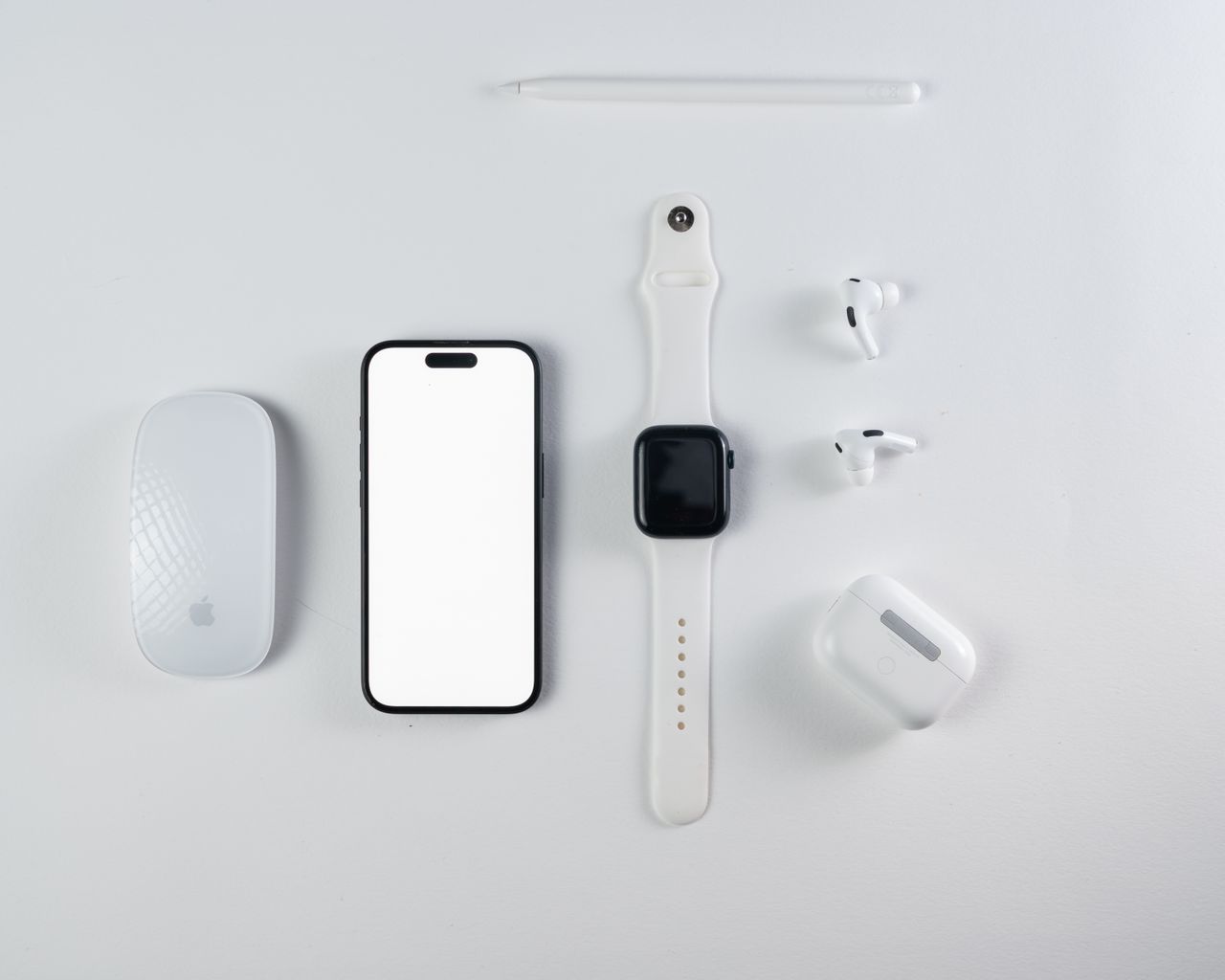 Services Minimalist flat lay of smartphone, smartwatch, wireless earbuds, and mouse on a white background.